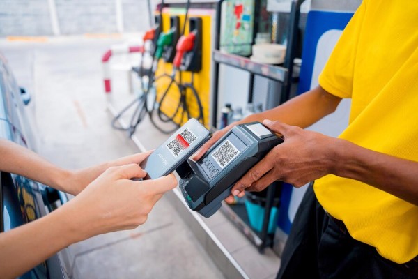 Why Gas Stations Need Smart Payment Solutions A Gas Station Employee in a Yellow Uniform Scanning a QR Code from a Customer's Smartphone Using a Handheld Payment Device