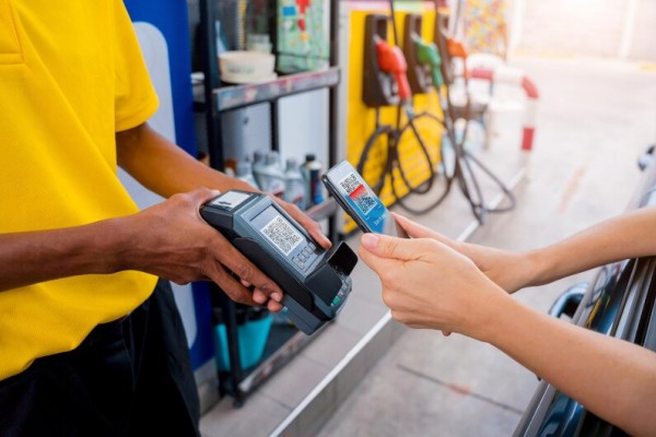 Optimized for Gas Stations and Convenience Stores A Customer at a Gas Station Using a Contactless Payment Method on a POS Terminal Held by an Attendant in a Yellow Uniform