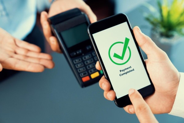 Reliable & Scalable Online Secure Payments A Person Holding a Smartphone Displaying a "Payment Completed" Confirmation While Using a Card Terminal for Digital Payment